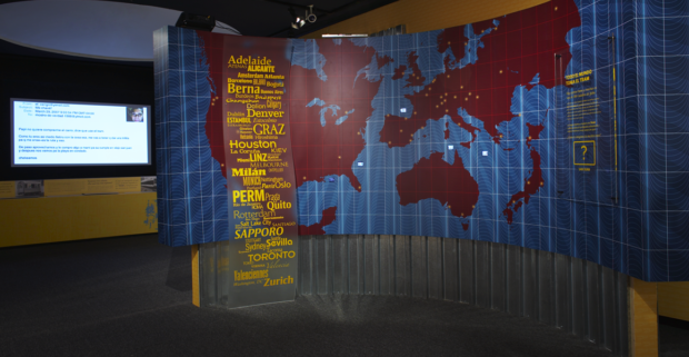 A sculptural map illustrates the cities, named in the scroll, that have Tram systems implemented. Videos of these are showcased in video ipods embedded in the map. The interactive screen projection can be seen on the far left of the image.